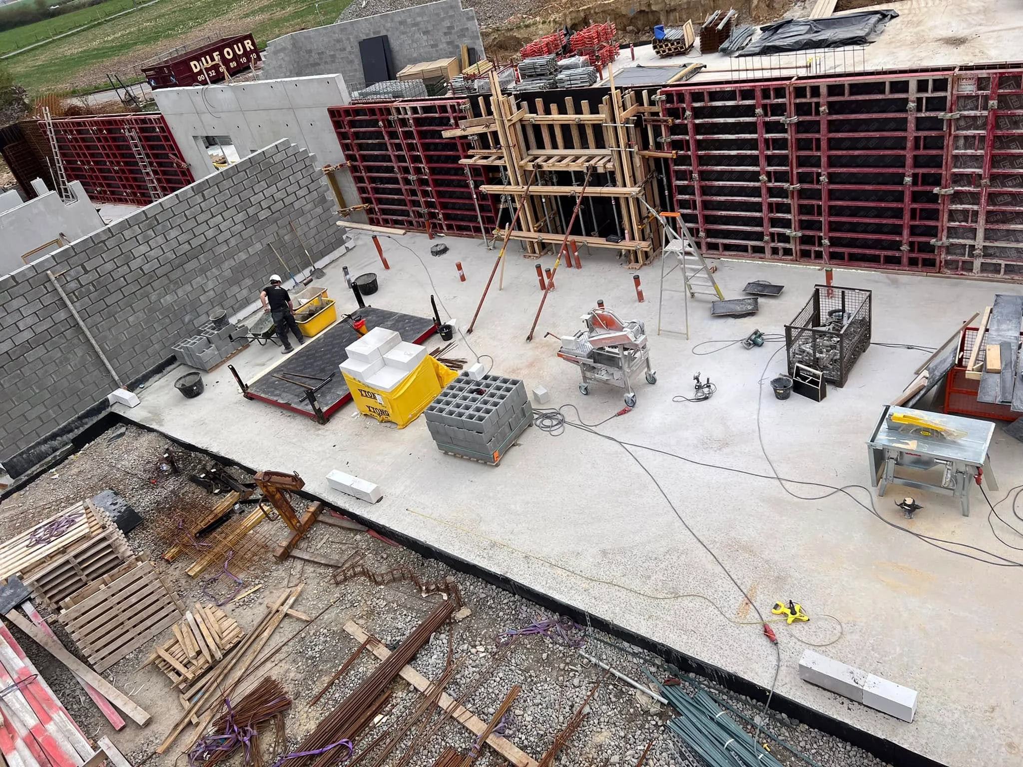 Zone de travail avec un mur en blocs, des coffrages et du matériel de maçonnerie